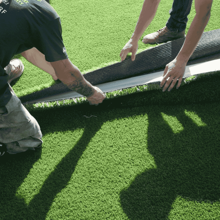 Two professional installers carefully joining and securing seams of artificial turf for a seamless finish.